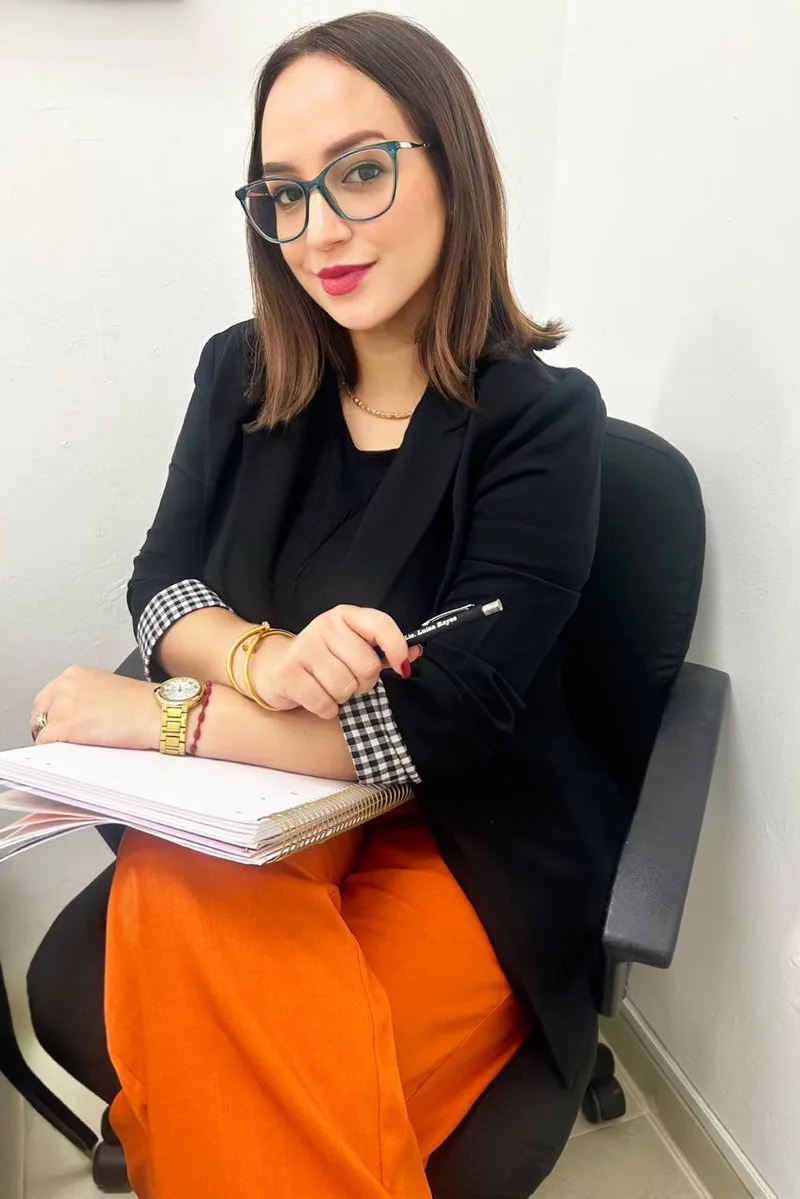 Luisa M. Reyes P. sentada con una libreta y un bolígrafo, mirando a la cámara