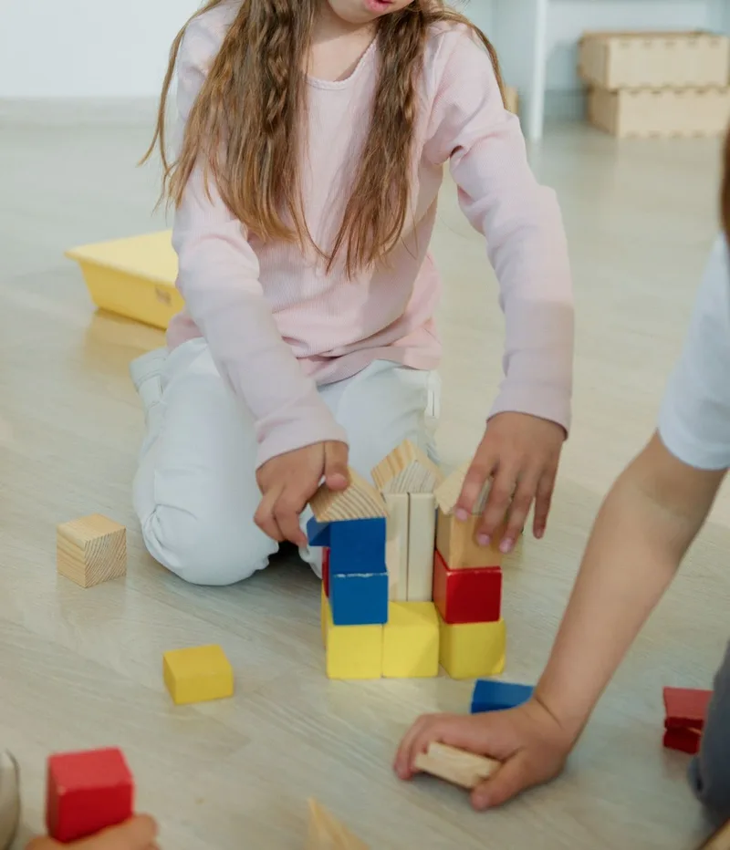 Imagen ilustrativa: niñas y niños construyen una torre con bloques de madera de colores sobre el piso